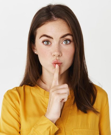 close-up-brunette-woman-hushing-tell-be-quiet-share-secret-looking-front-showing-taboo-sign-while-standing-white-wall_176420-42639